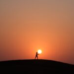 silhouette of person standing on hill during sunset